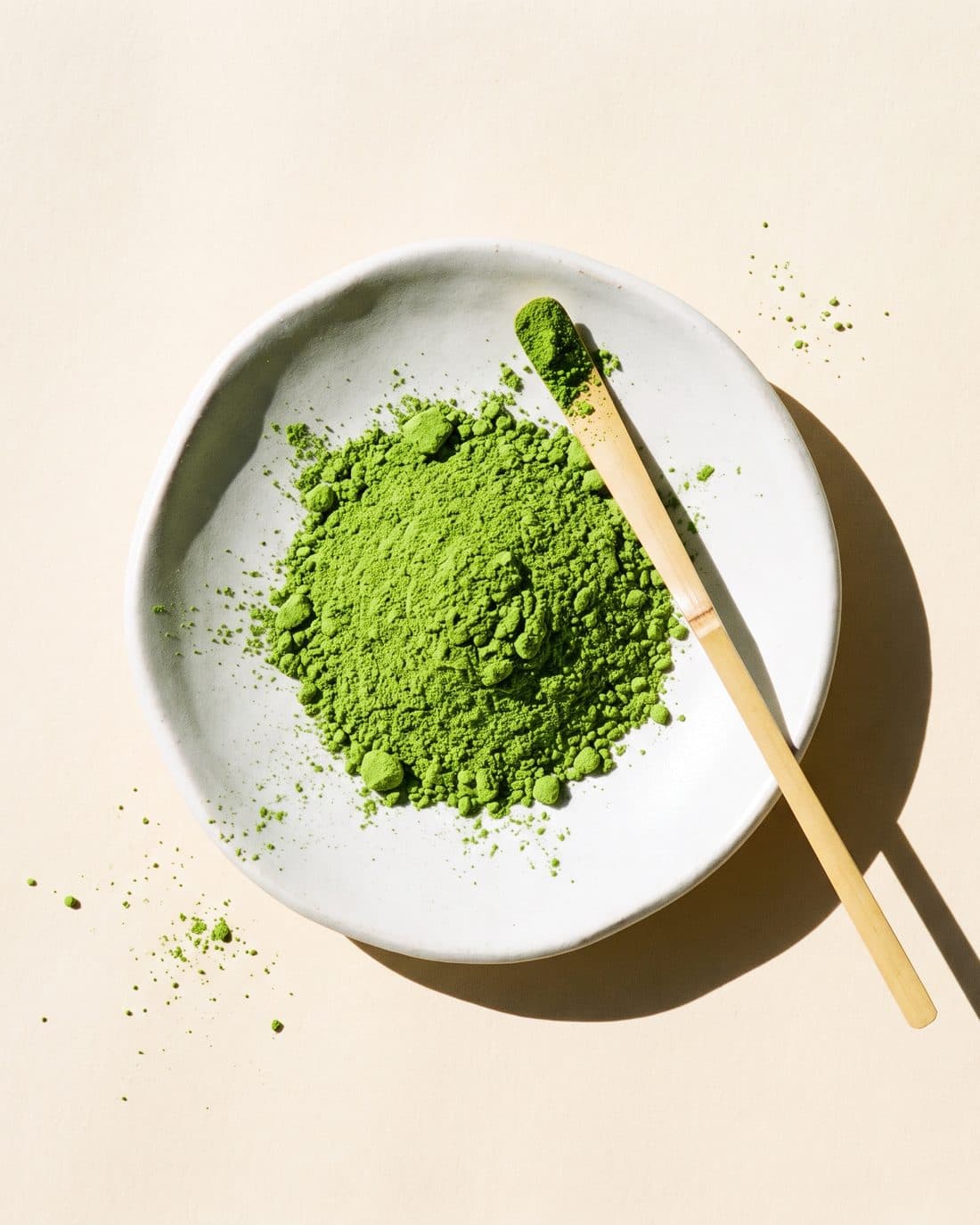 Krem kağıt üstünde beyaz tabakta parlak yeşil matcha tozu ve bambu kaşık